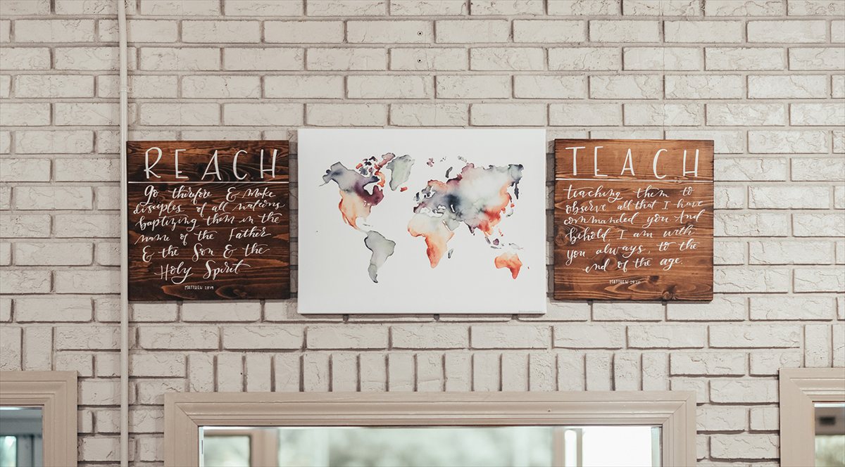 Two hand-lettered wooden signs in the Oasis lobby reading Reach and Teach, on either side of a watercolor world map