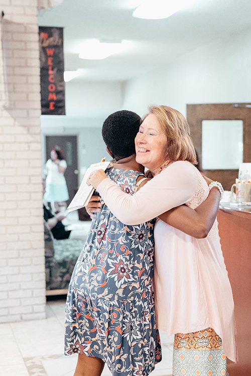 Two women hugging warmly in the Oasis lobby beneath a welcome banner